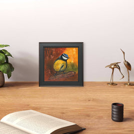 Office space with a book and a plant featuring a framed painting of a blue tit.