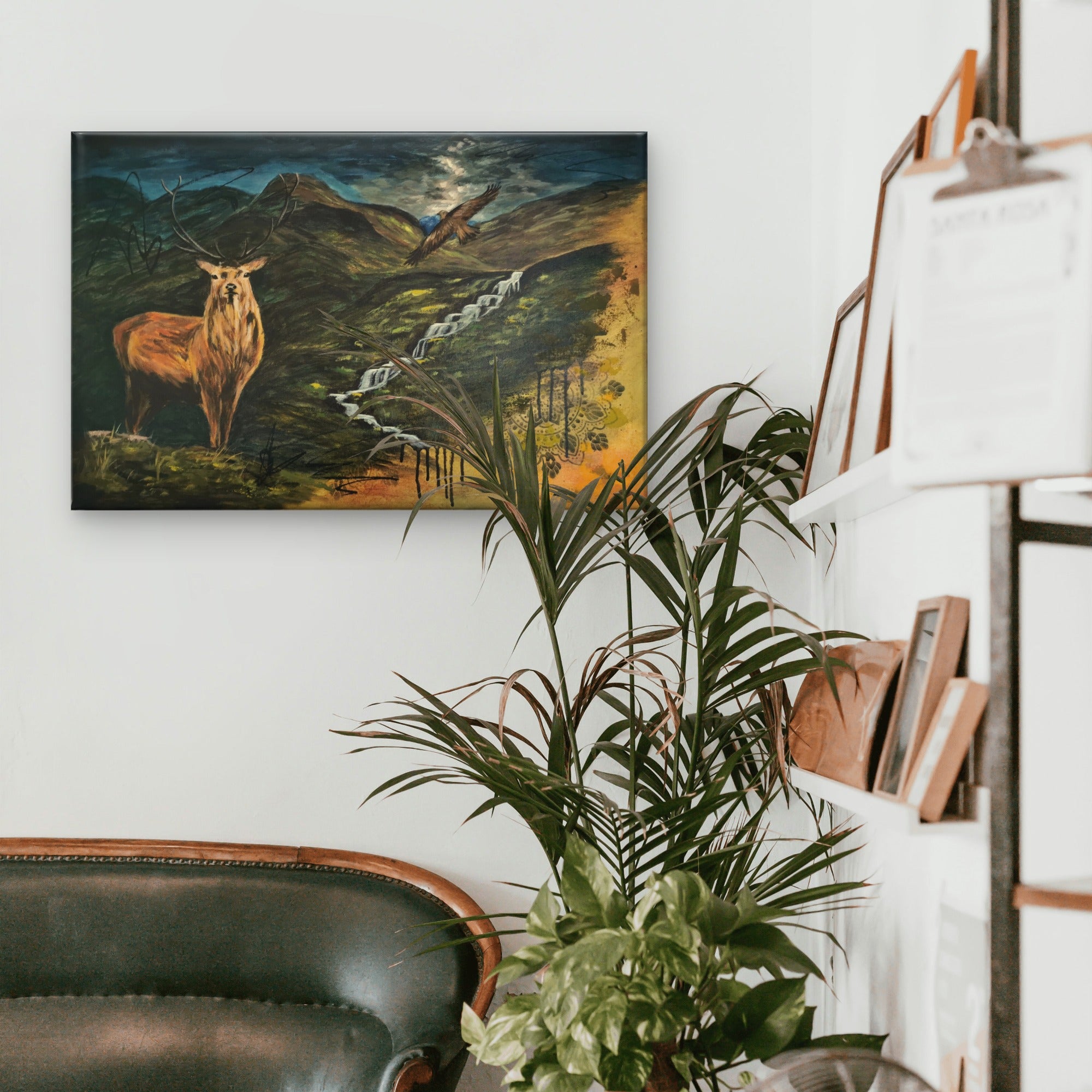 A room with a sofa, a bookshelf, and a plants featuring a painting of a stag and dramatic Scottish landscape